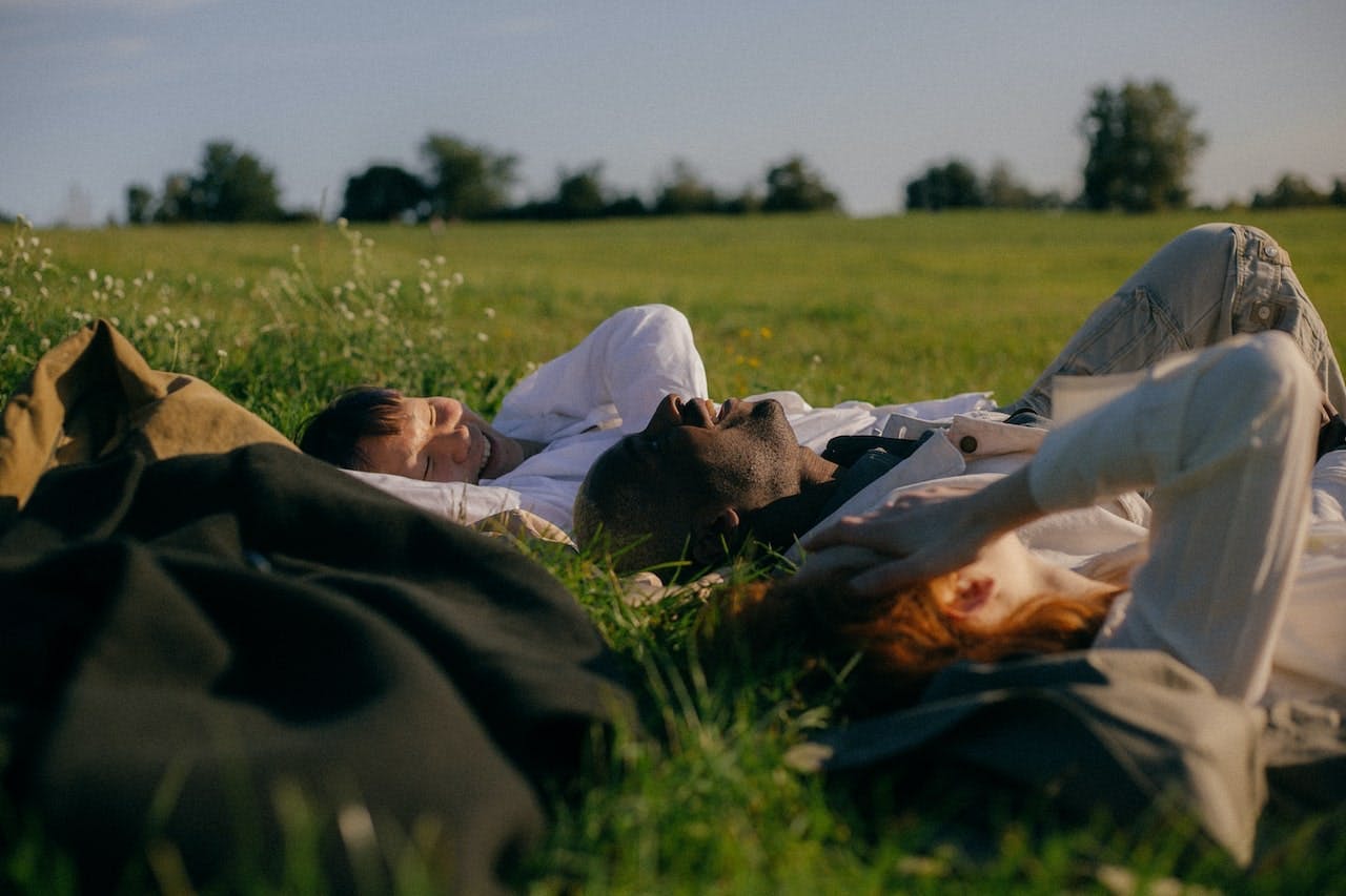 three friends lying in a grassy field and laughing