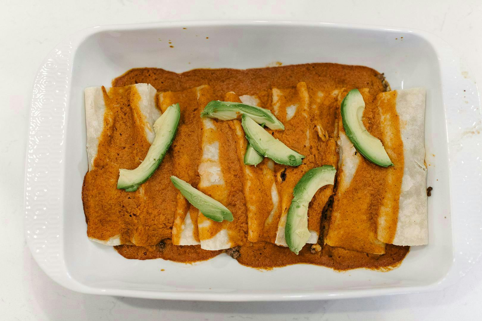 beef enchiladas with avocado in baking dish