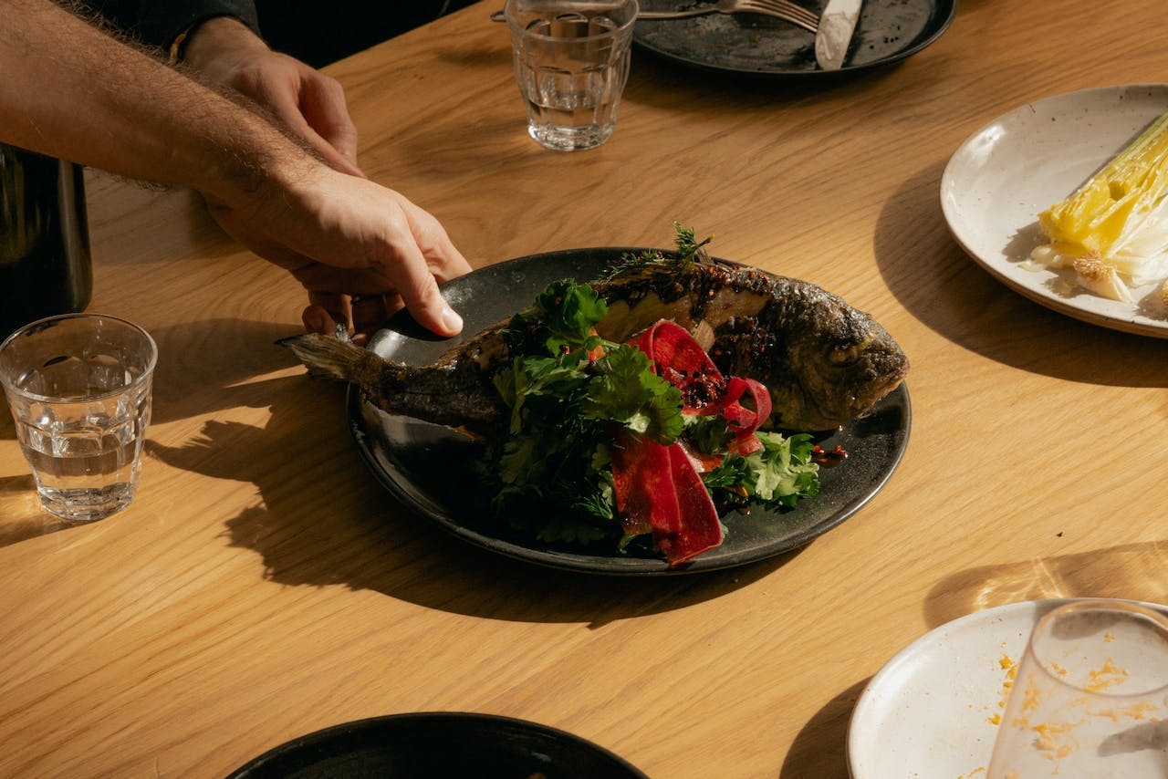 person placing a micronutrient-rich salad with fish and vegetables on a dining table alongside other dishes