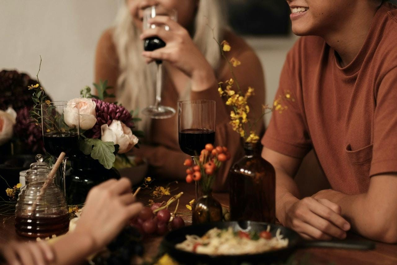 group of young individuals sitting at a table and eating a holiday dinner with wine
