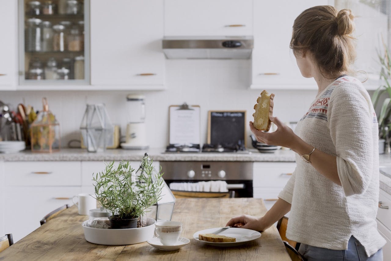woman standing in her kitchen and eating a slice of toast
