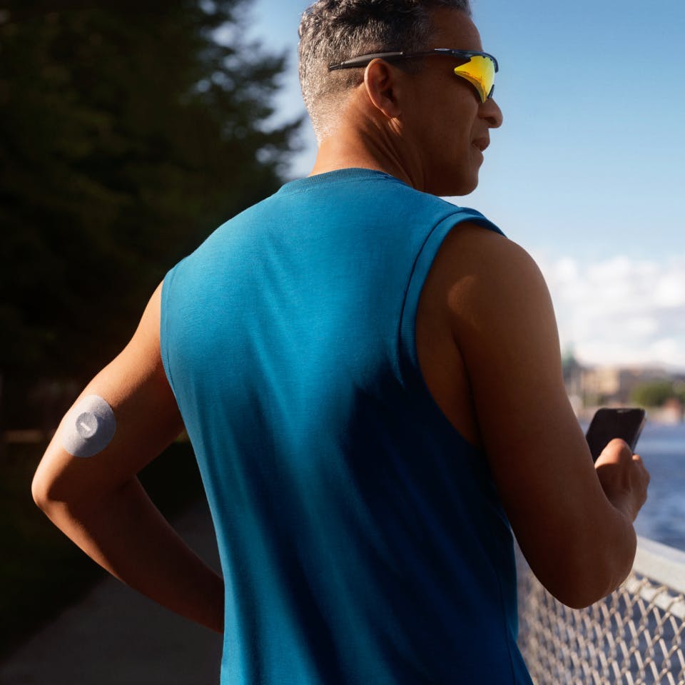 A man with sunglasses takes a break from running to scan his CGM continuous glucose monitor with the Veri app on his iPhone