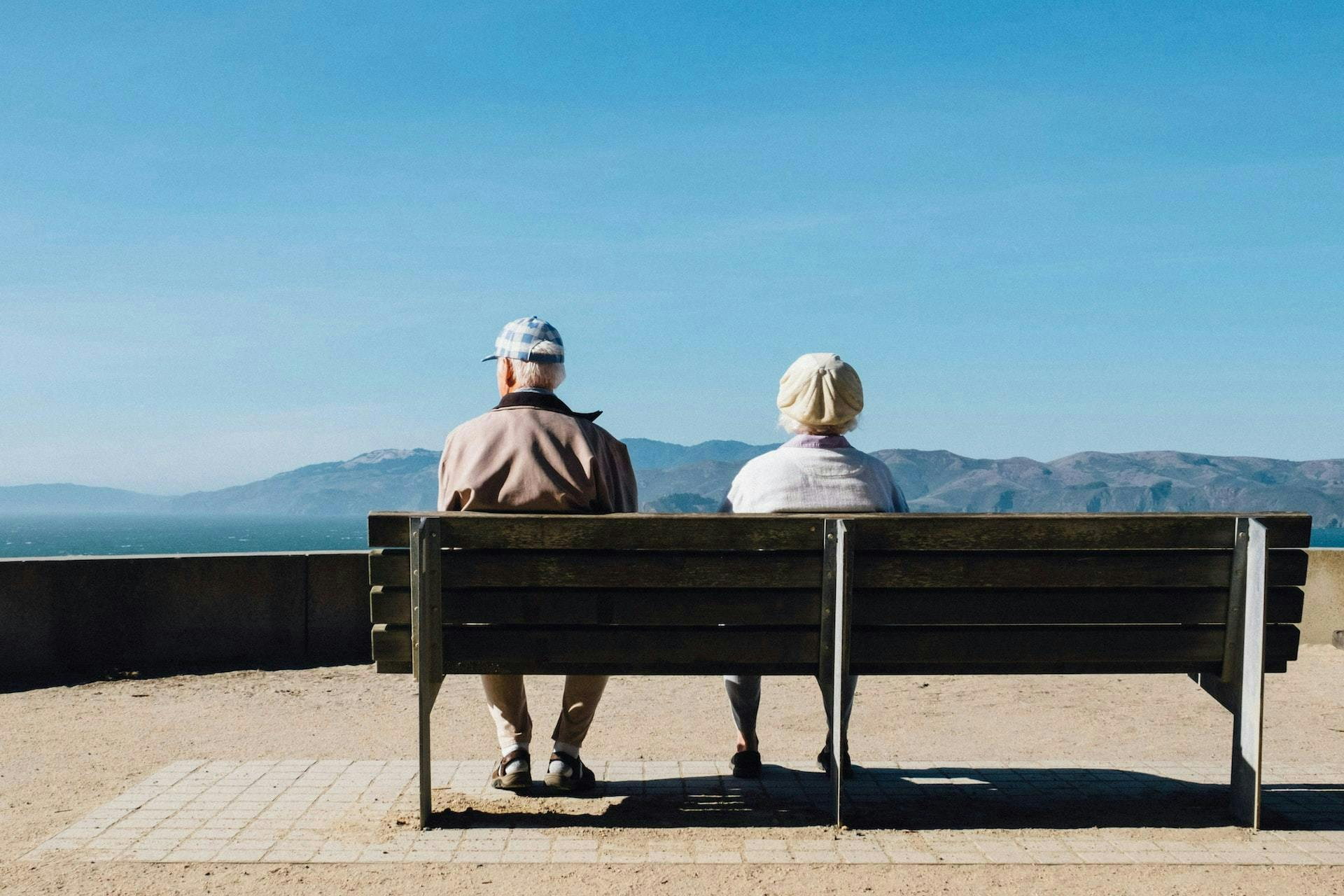 elderly couple sitting on a bench and looking out at the mountains