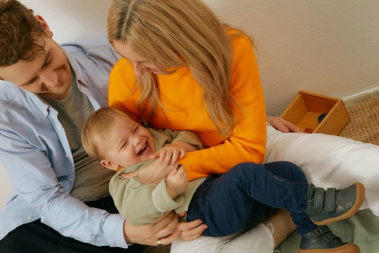 a young man and woman sitting in a living room and holding their son