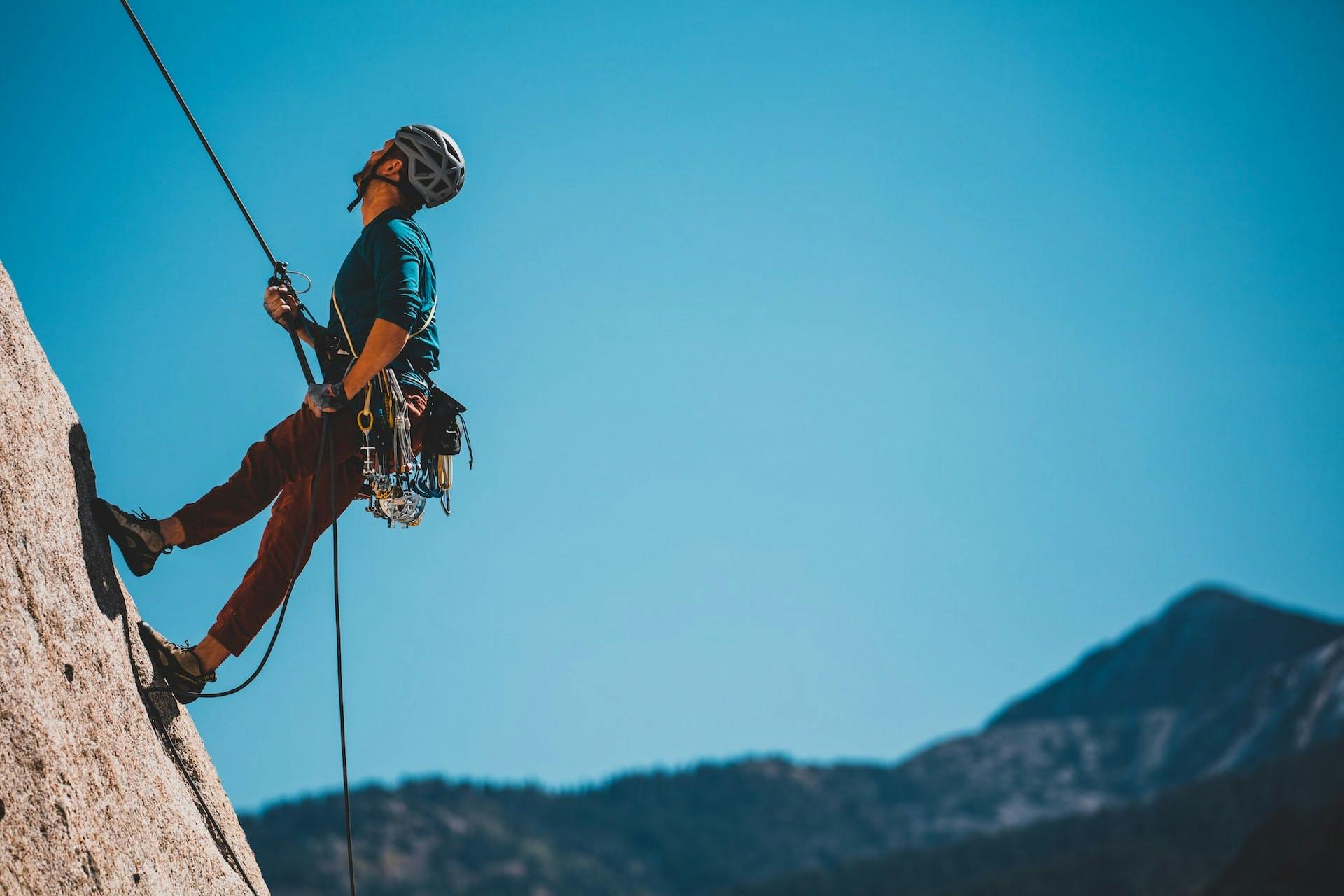 man in helmet and gear using a rope to climb a mountain