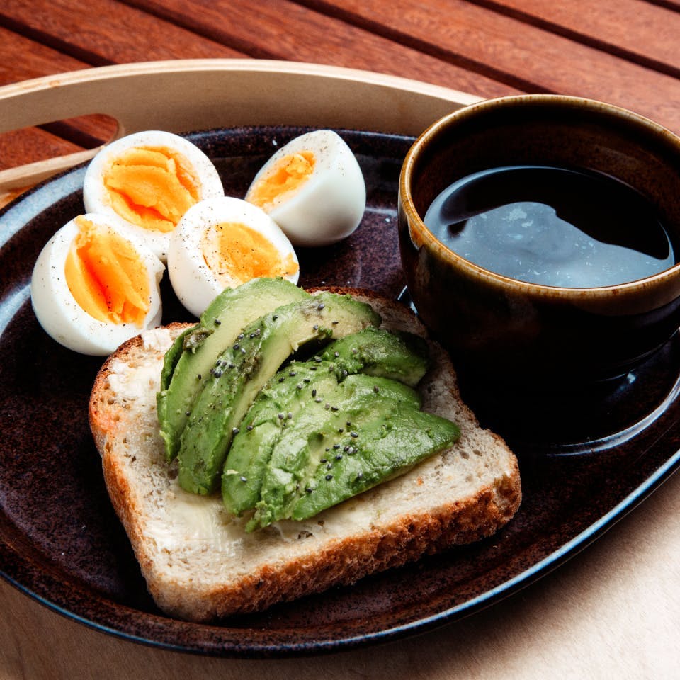 A plate with a healthy breakfast of two hard boiled eggs, avocado toast and tea