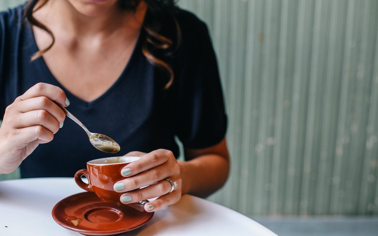 woman at coffee shop stirring sweetener into espresso