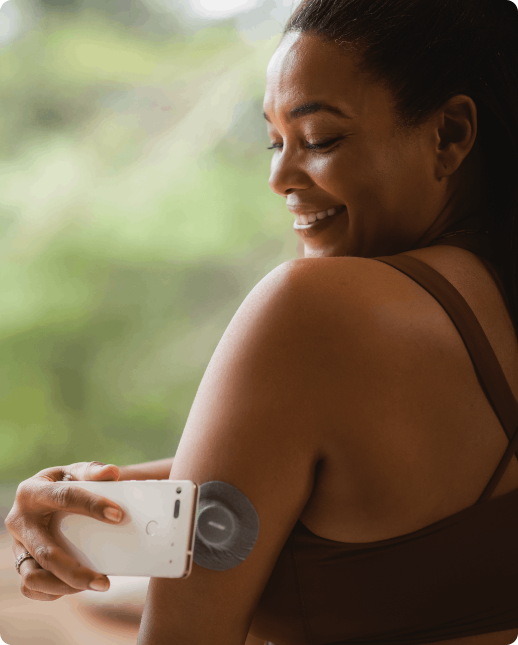 A middle-aged black woman scans the Veri CGM on her arm, using her Android smartphone