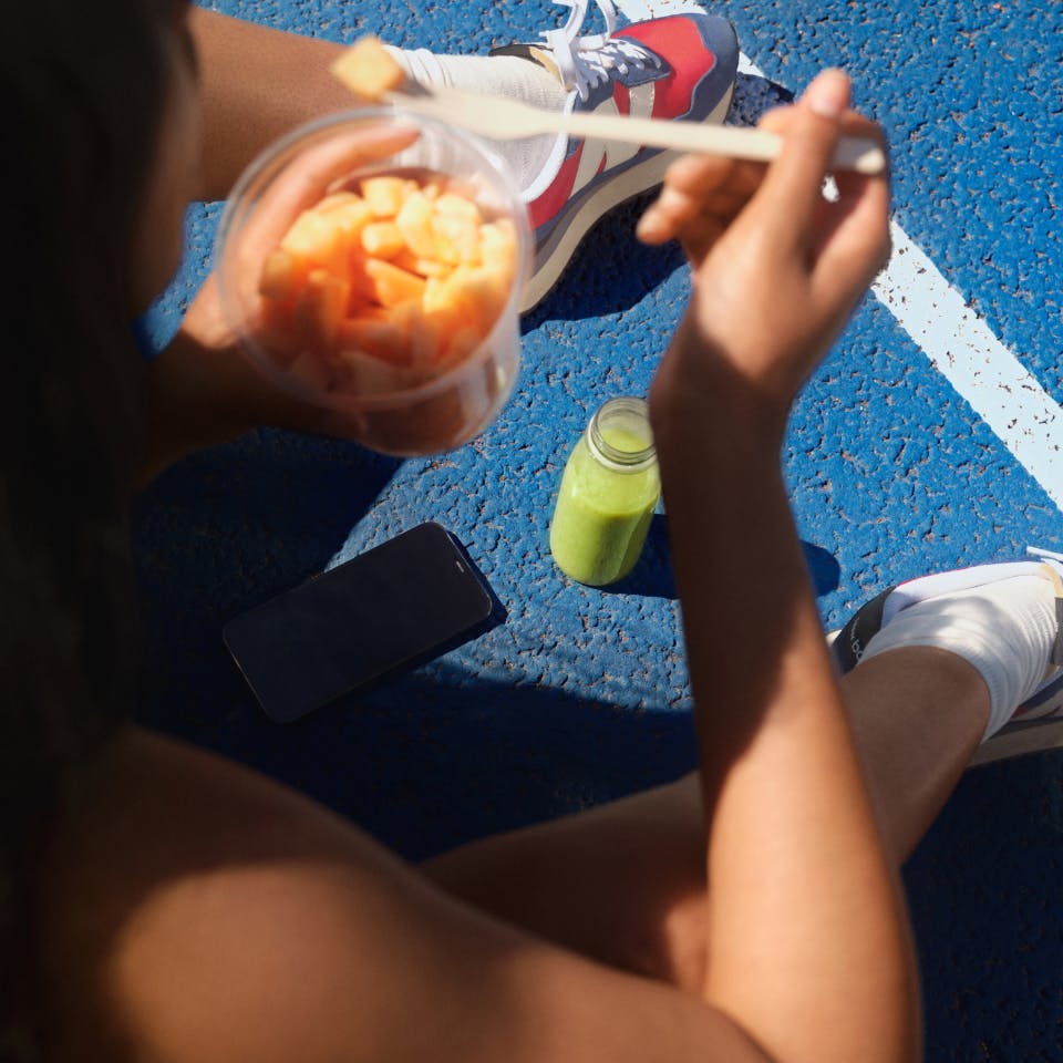 person eating fruit on tennis court 